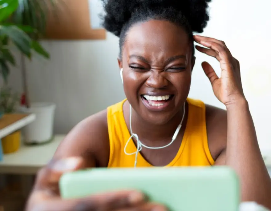 A woman with earbuds laughs at her phone on a video call.