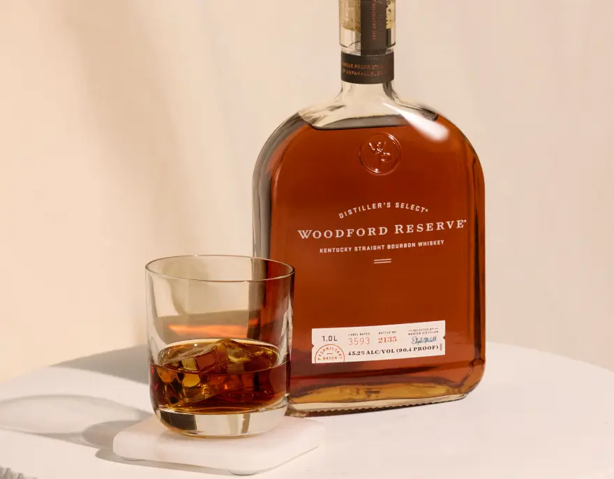 A bottle of Woodford Reserve beside a glass of bourbon over ice.
