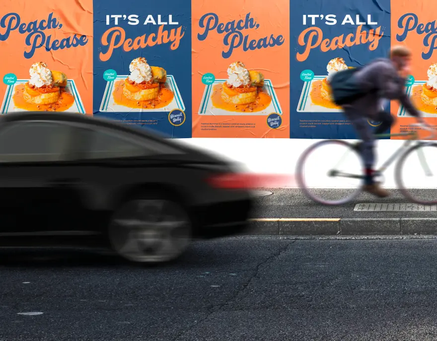 A wall of “Peach, Please” and “It’s All Peachy” posters behind a passing car and cyclist.