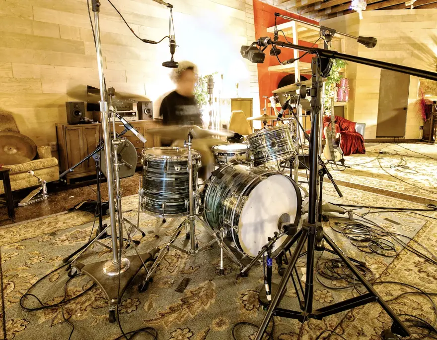 A drum kit and microphones set up in a warm, rug-lined recording studio.