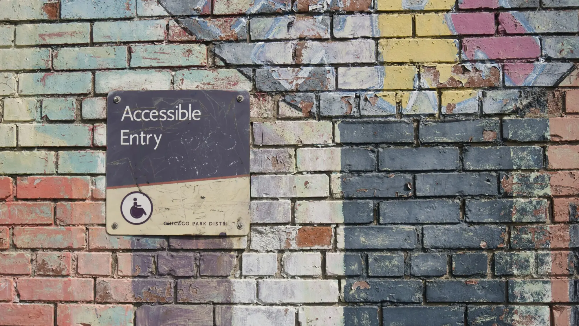 Accessible Entry sign with wheelchair symbol mounted on a colorful painted brick wall, representing accessibility in public spaces