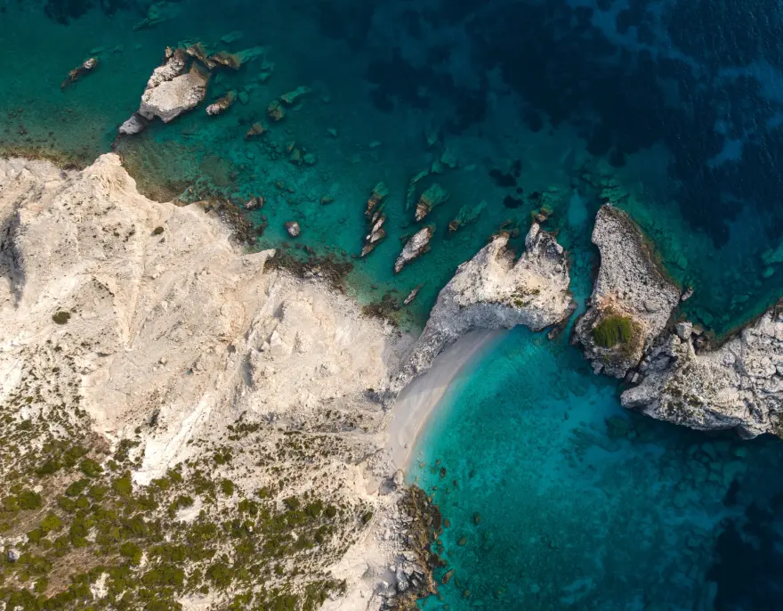 A rocky white coastline from above, turquoise water in its coves.
